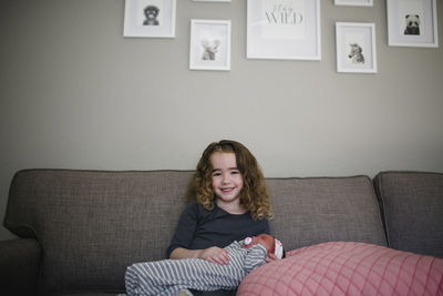 Portrait of cheerful girl with sister sitting on sofa at home