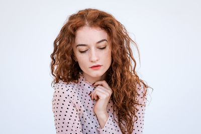 Portrait of a sad young woman with red hair close-up, downcast eyes on a light background