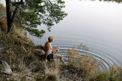 High angle view of shirtless man sitting at lakeshore