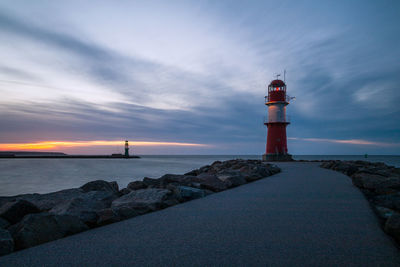 Lighthouse by sea against sky at sunset