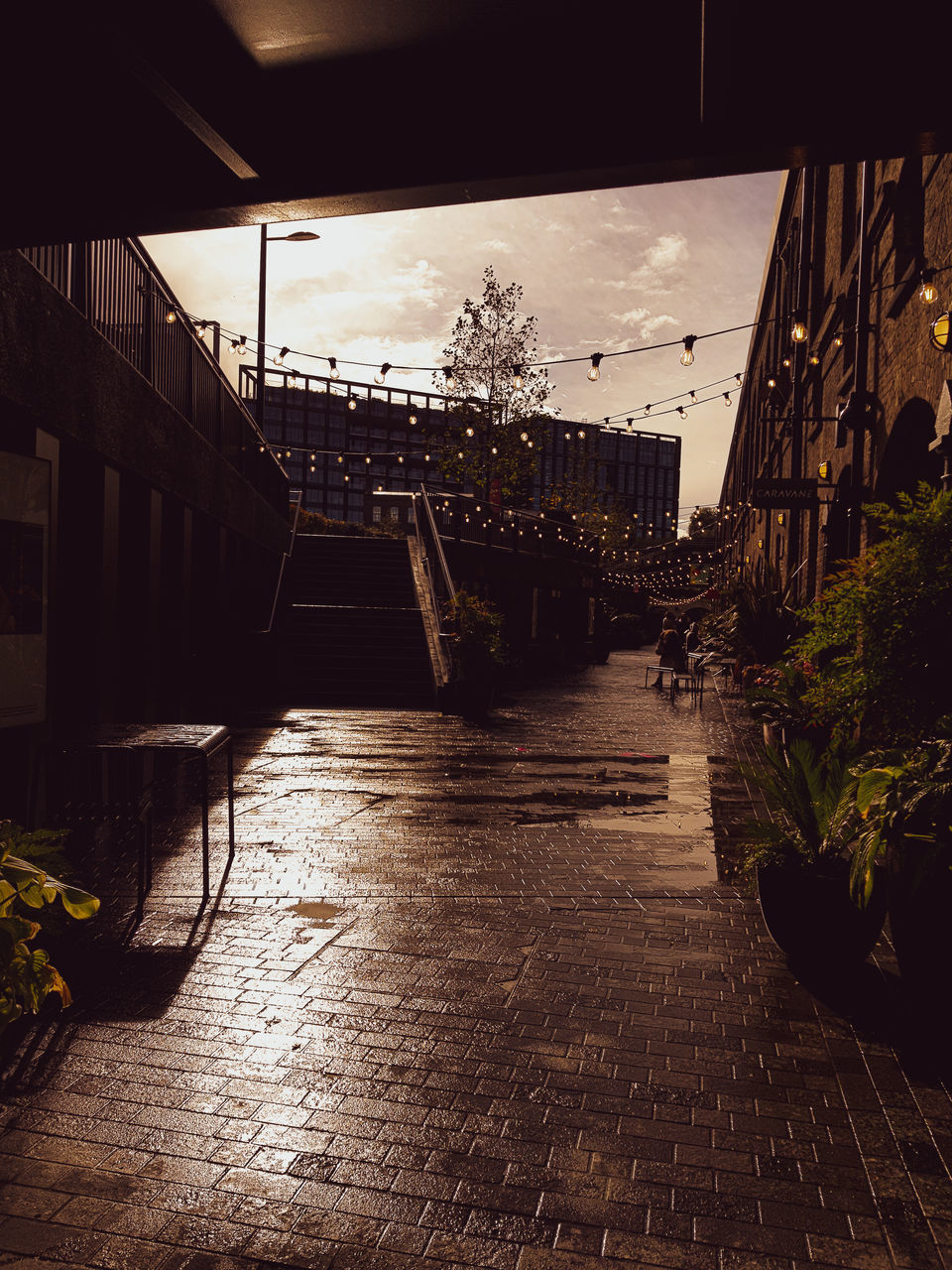 WET FOOTPATH AMIDST BUILDINGS AGAINST SKY IN CITY