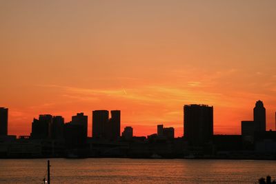 Silhouette buildings in front of calm sea at sunset