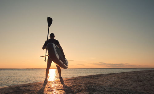 Silhouette man on beach against sky during sunset