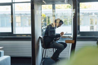 Businessman writing on clipboard in soundproof cabin at office