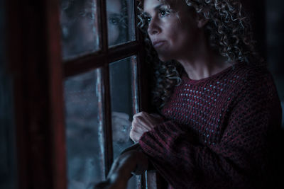 Portrait of young woman standing against window