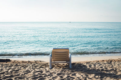 Empty lounge chair on shore at beach against sky
