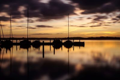 Silhouette sailboats on lake against sky at sunset