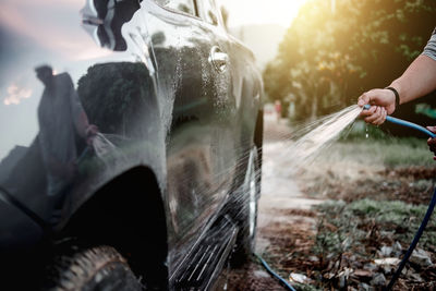 Cropped hand spraying water on car at field