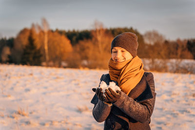 Smiling woman in a scarf and hat holds a handful of snow in winter