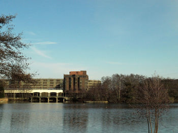Buildings by lake against clear blue sky