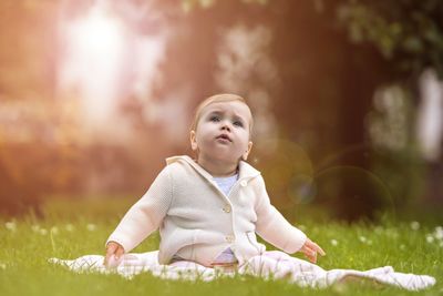 Cute boy looking away while sitting on field