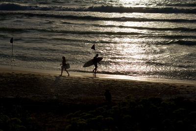 Silhouette people standing at beach during sunset