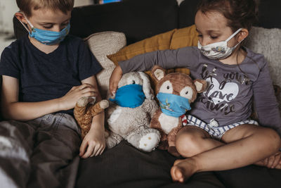 Young girl and young boy with masks playing with animals on couch