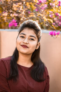 Portrait of young woman smiling while standing against pink flowers