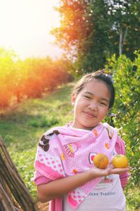 Cute girl holding fruit while standing on tree