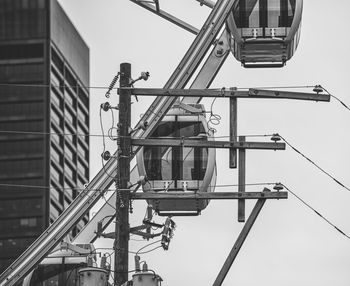 Low angle view of electricity pylon by ferris wheel against sky