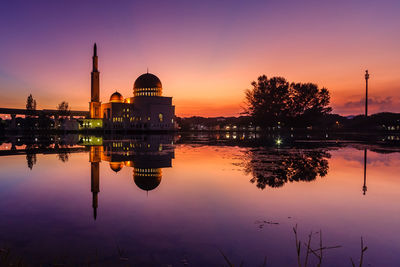 Reflection of illuminated buildings in lake against sky during sunset