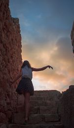 Low angle view of woman standing on rock against sky