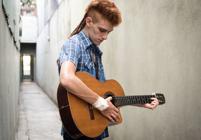 Young man playing guitar against wall