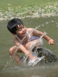 Boy splashing water while sitting on rock in river