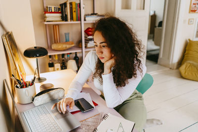 Young woman with curly hair using laptop while studying at home