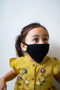 Cute girl wearing mask sitting by wall