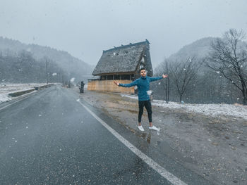 Portrait of man with arms outstretched standing on road during winter