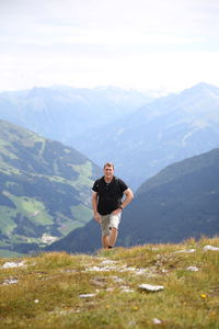 Portrait of male hiker walking on mountain against cloudy sky