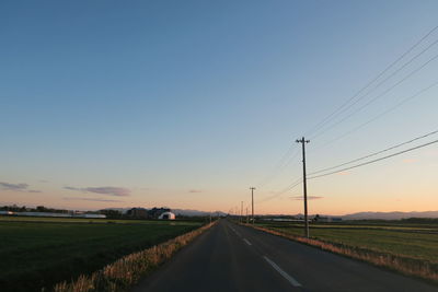 Road by field against sky during sunset