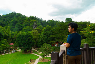 Side view of man sitting on bench against trees