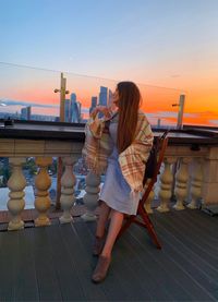 Woman standing by railing against sky during sunset