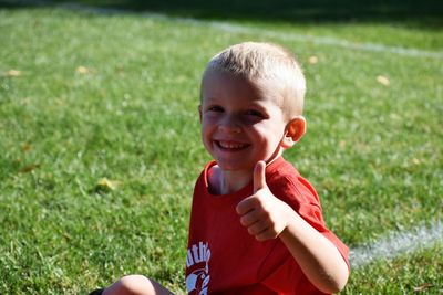 Portrait of happy boy gesturing thumbs up while sitting on playing field
