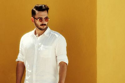 Portrait of young man standing against yellow wall