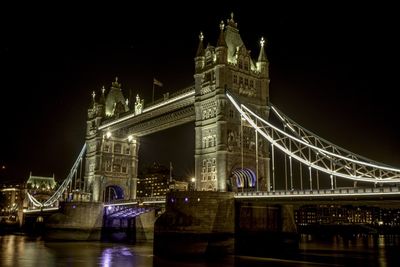 Illuminated tower bridge over river against at night