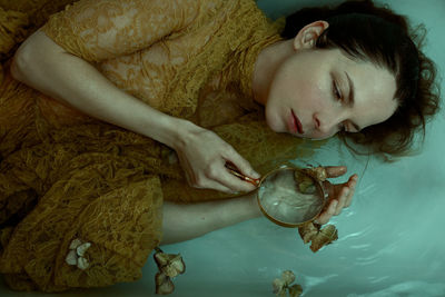 The mermaid - selfportrait - woman with a lace dress lying in water with a magnifier in her hands