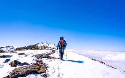 Man standing on snow covered mountain against blue sky