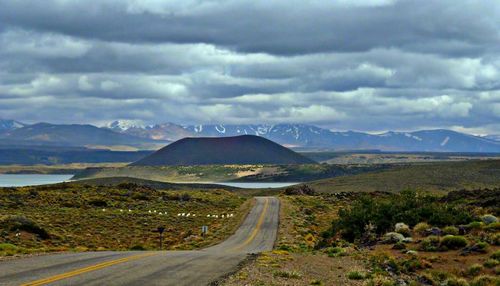 Scenic view of road by mountains against cloudy sky