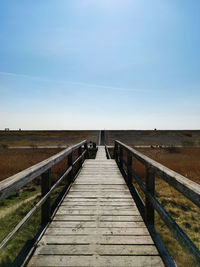 View of wooden footbridge leading to bridge against sky