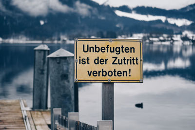 Warning sign on wooden post by lake