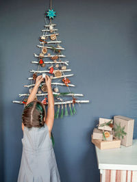 Rear view of girl decorating christmas tree hanging on wall