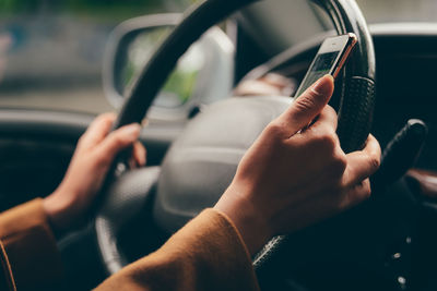 Cropped hands holding smart phone while driving car