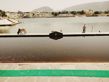 People on lake by mountain against sky