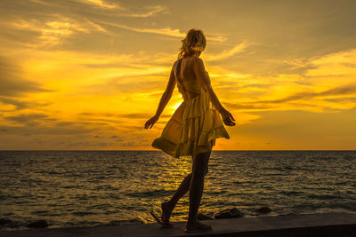 Woman walking at beach against sky during sunset