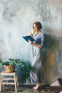 Woman reading book against wall