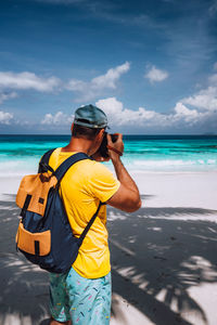 Rear view of man photographing with camera while standing at beach