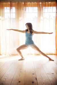 Woman doing yoga against window at home during sunny day