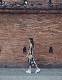 Full length of a girl standing against brick wall