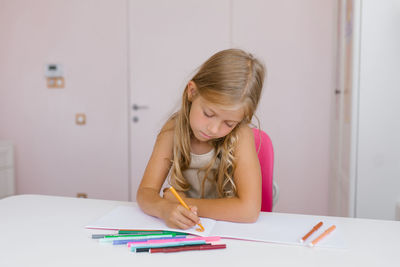Caucasian schoolgirl child seven years old is engaged in distance learning, drawing lessons