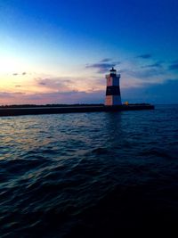 Lighthouse by sea against sky during sunset