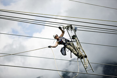 Low angle view of man working on cable against sky